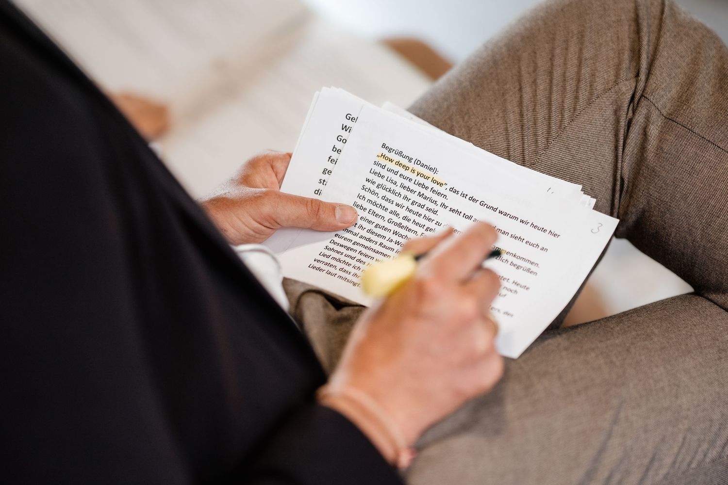 Person highlighting text on printed documents while sitting in a chair, reviewing written content with a yellow marker.