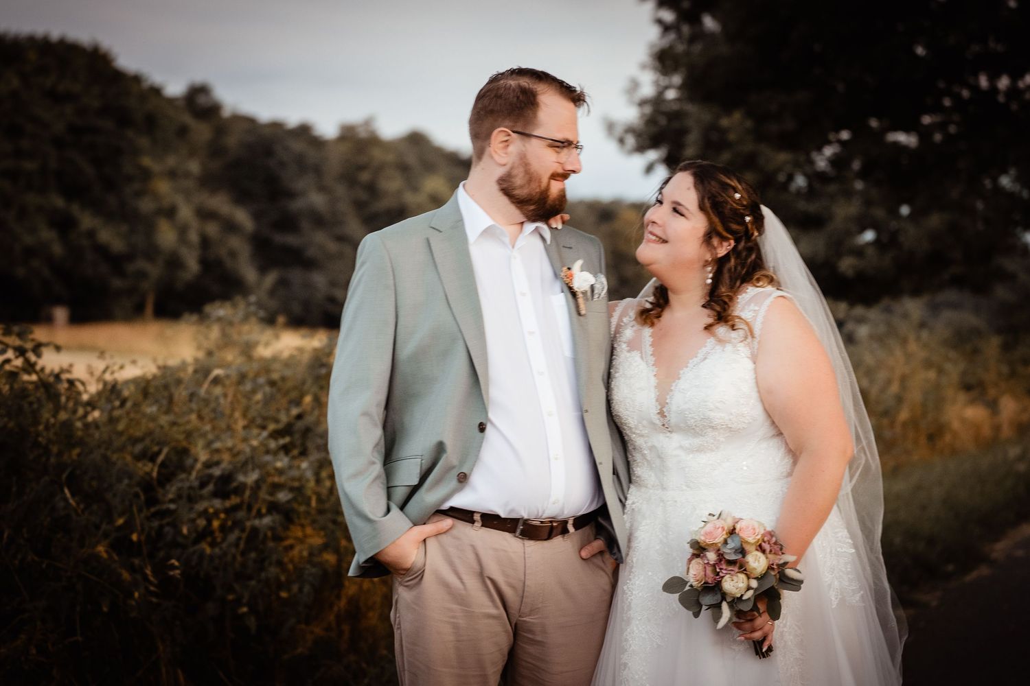 Bride and groom smiling at each other in golden hour light at outdoor wedding portrait session.