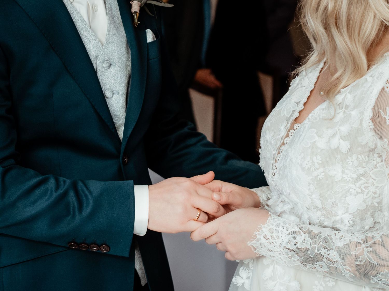 Bride and groom exchanging rings during wedding ceremony, close-up of hands in elegant attire.
