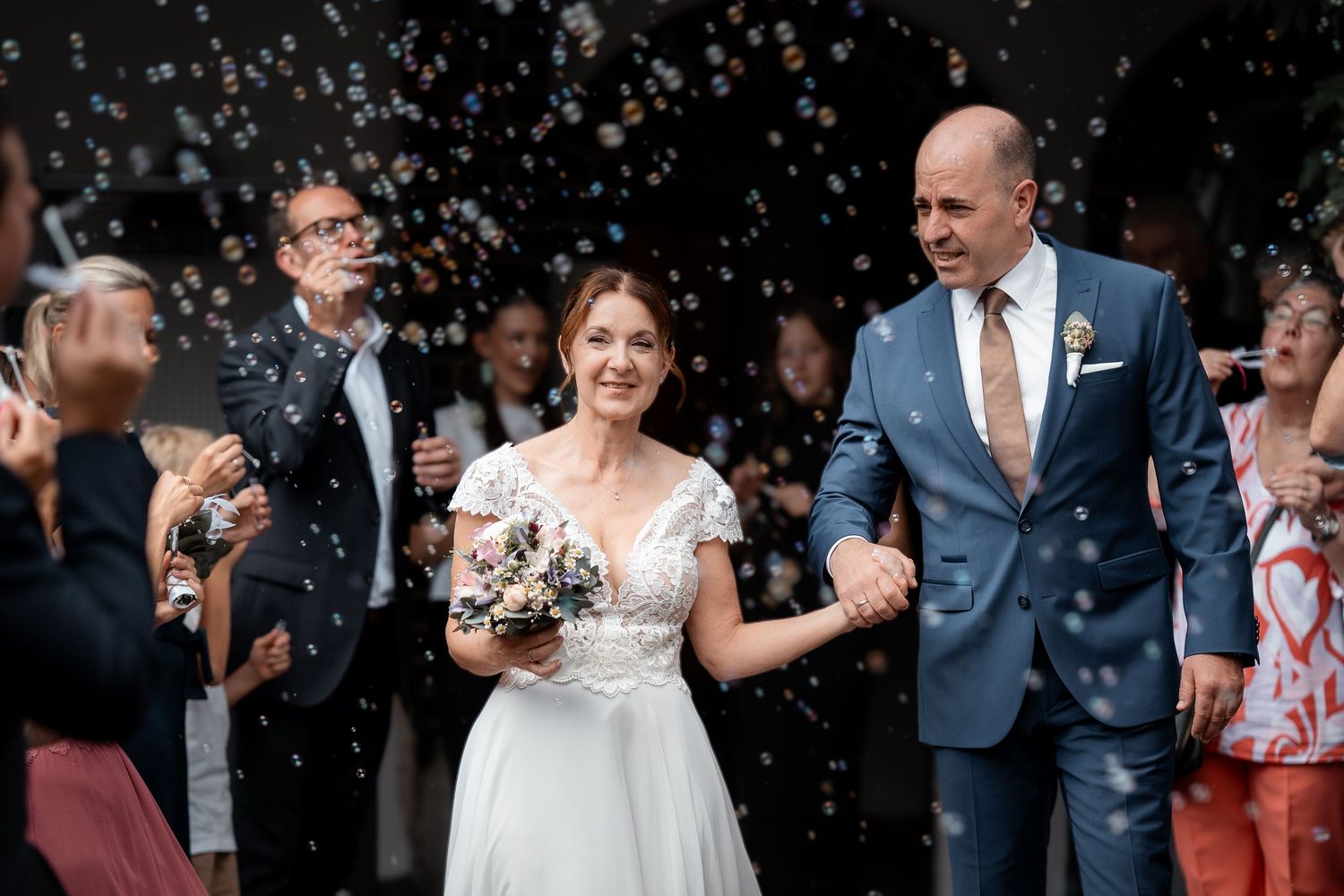 Newlyweds exit the ceremony as joyful guests blow bubbles around them in celebration.