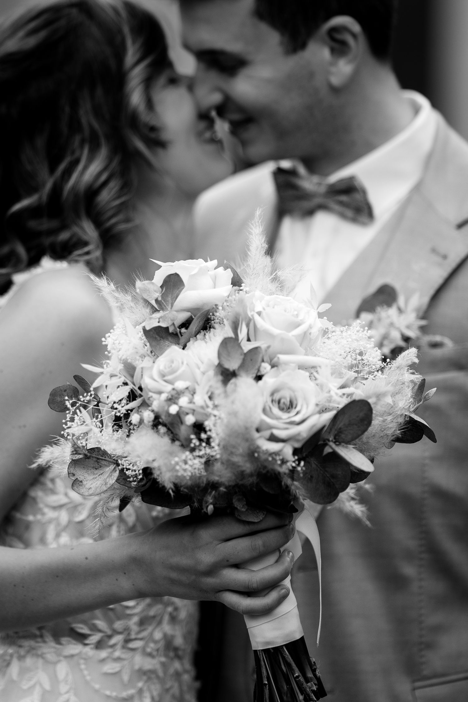 Black and white wedding photo of bride and groom almost kissing while holding a bouquet of roses.
