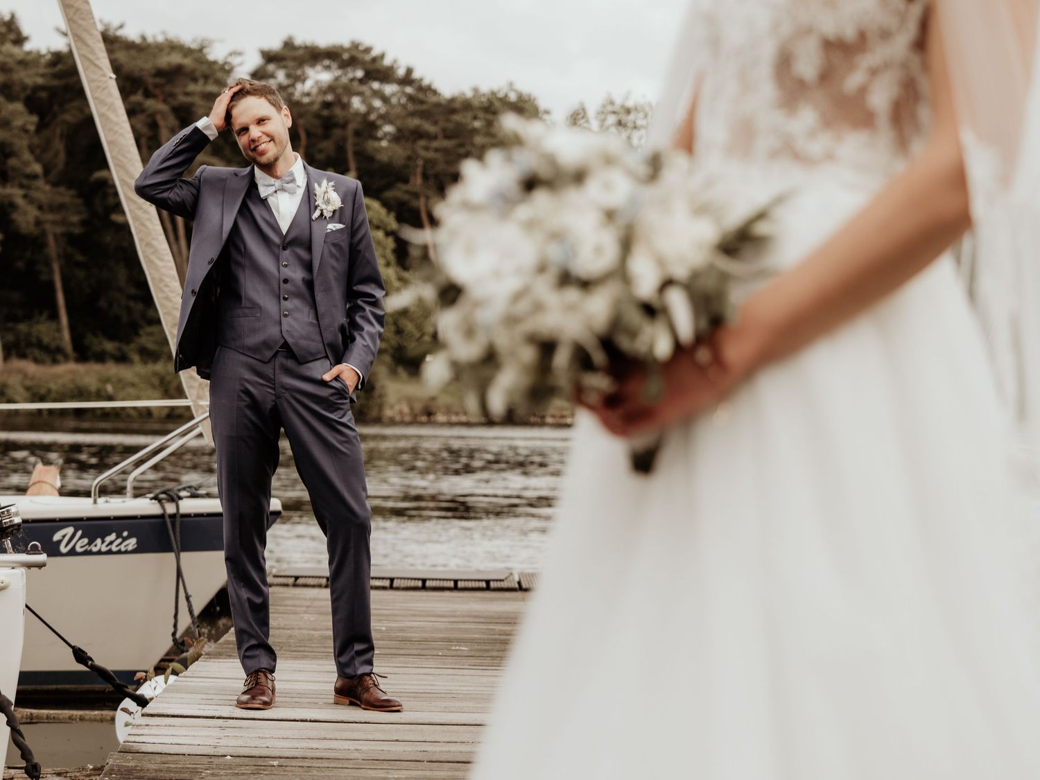 A wedding photo on a dock showing a suited figure and a white wedding dress with bouquet in the foreground.