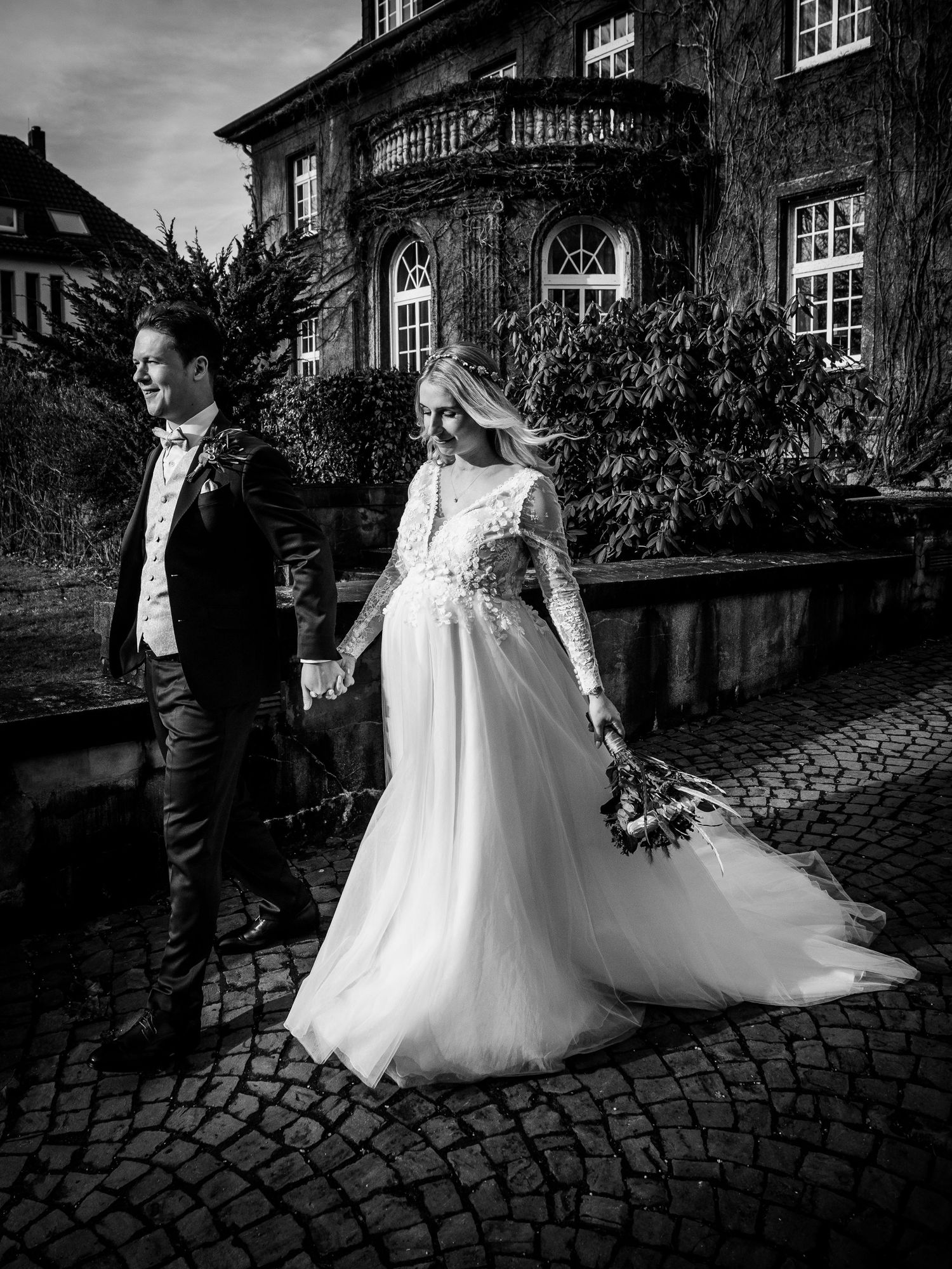 Bride and groom holding hands outside a grand ivy-covered building in a stunning black and white portrait.