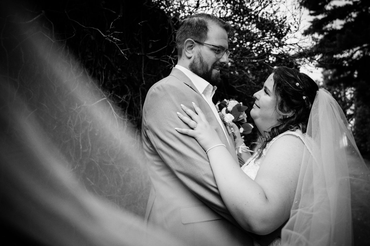 Black and white romantic wedding portrait of bride and groom gazing at each other beneath a veil.