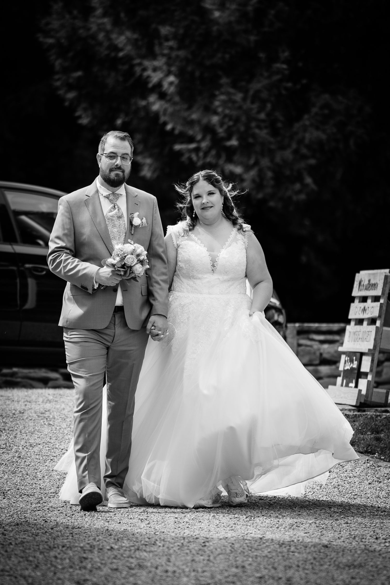 Black and white photo of a smiling bride and groom walking together on their wedding day, bride in ballgown.