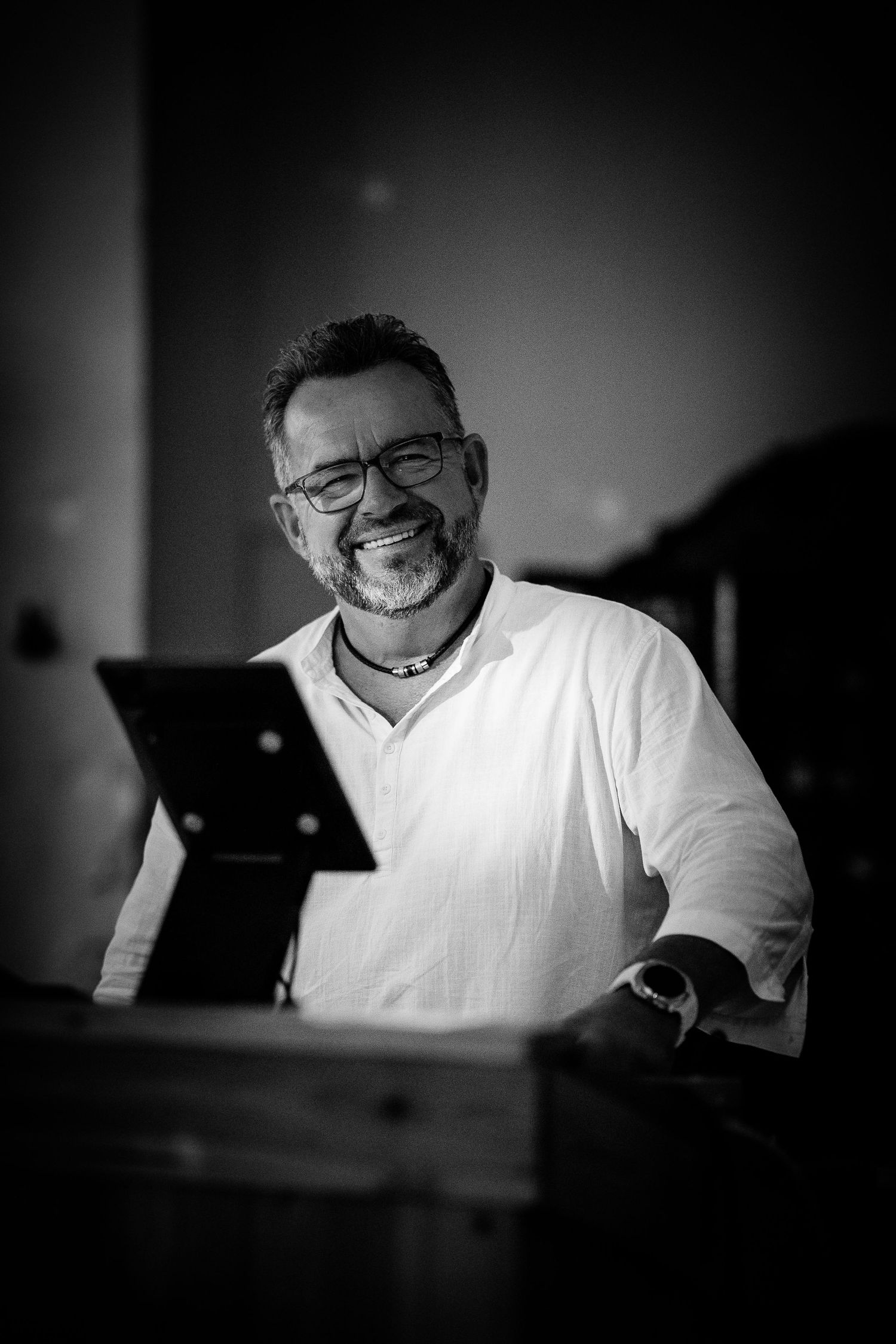 Smiling middle-aged man with glasses and beard reading at a podium in black and white photo.
