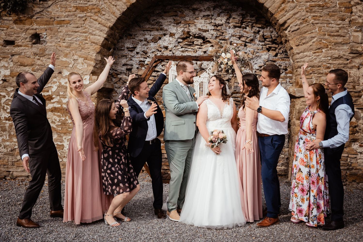 Wedding party posing and celebrating in front of a stone arch with floral decoration.