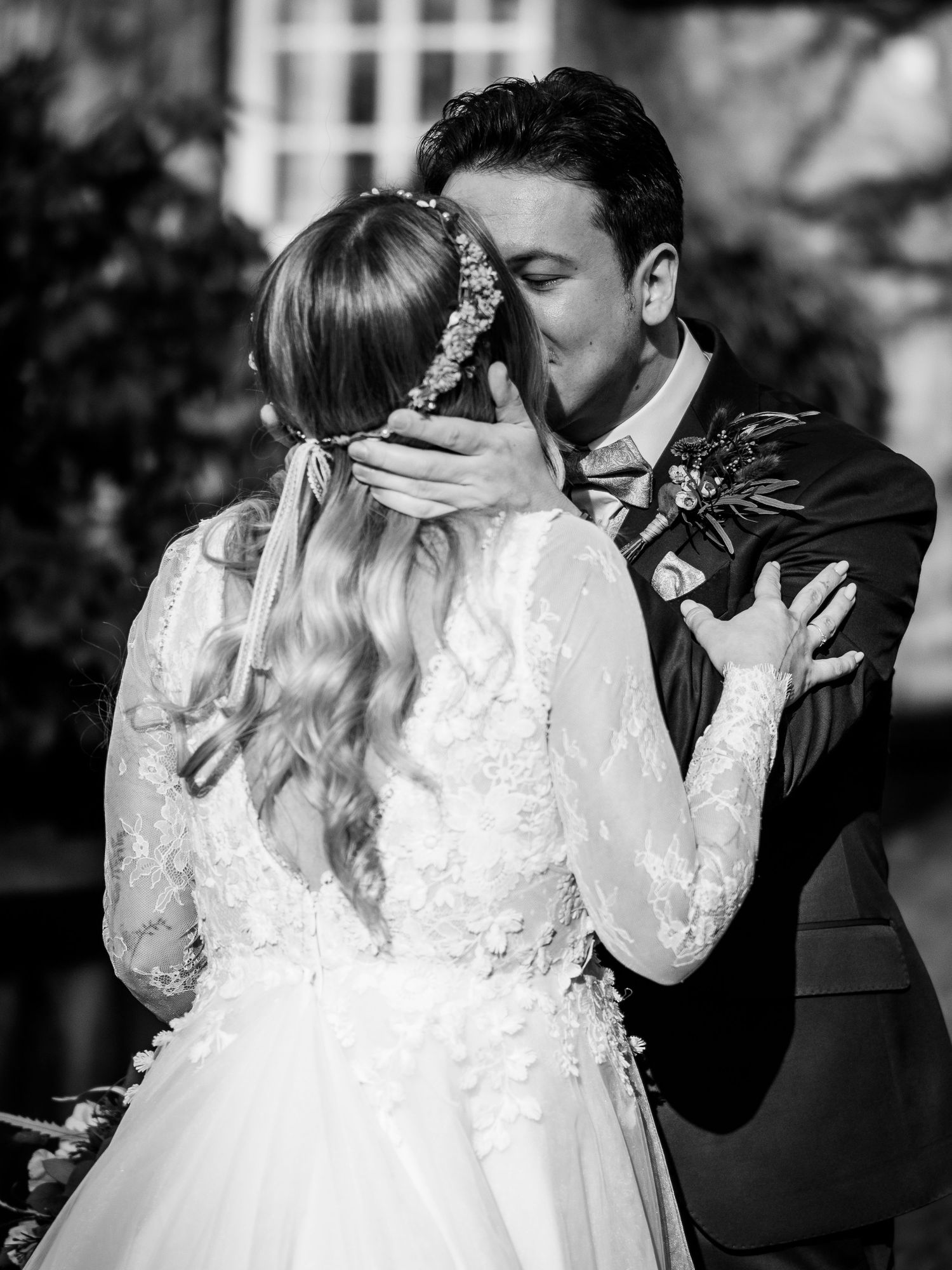 Black and white photo of bride and groom sharing their first kiss at wedding ceremony, bride in lace dress.