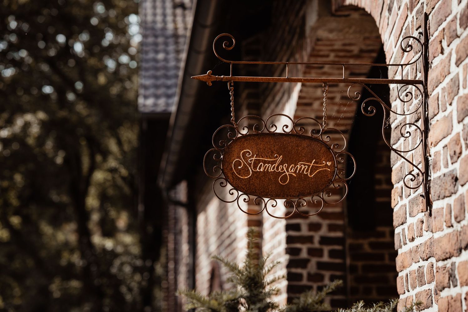 Ornate wrought iron sign reading Standesamt hanging on a rustic brick wall with arched doorway.