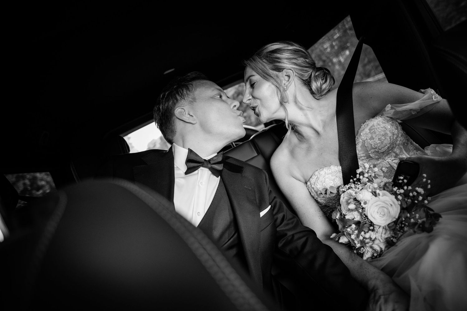 Bride and groom sharing an intimate kiss inside a car after their wedding ceremony.