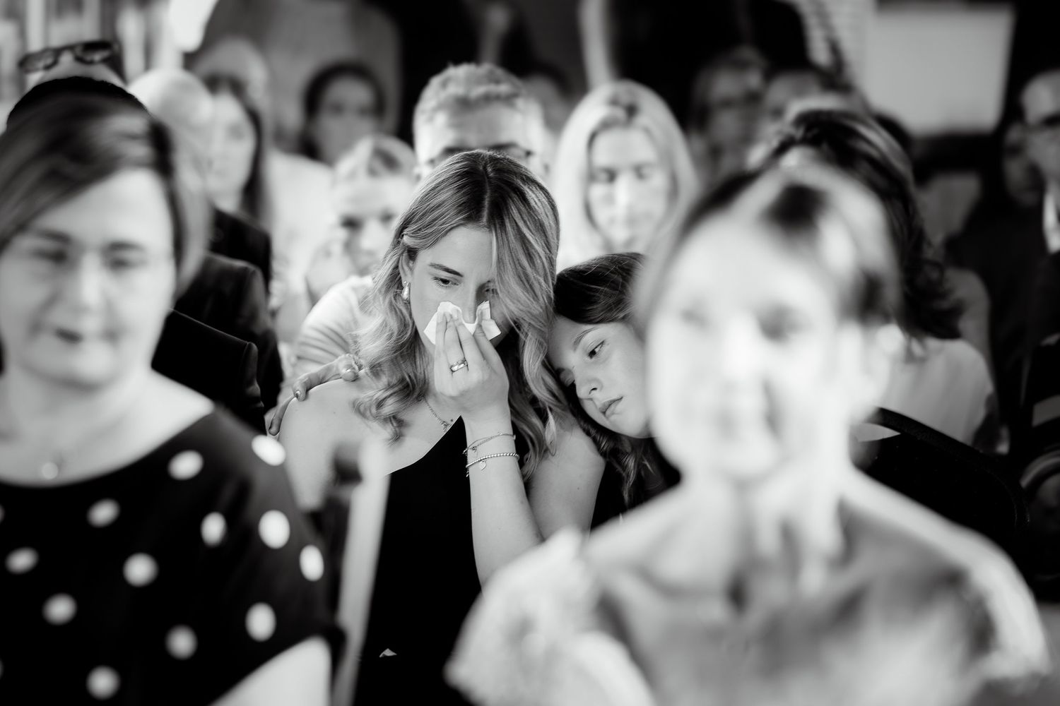 Emotional wedding guest wiping tears during ceremony in black and white photo.
