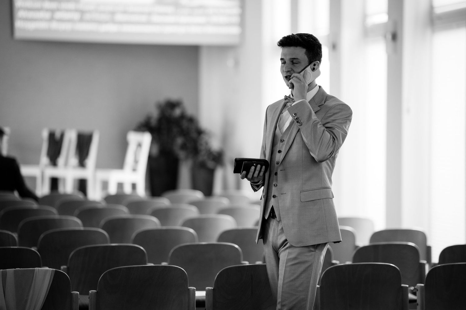 Man in suit wearing mask holds tablet in empty conference room, black and white photo.