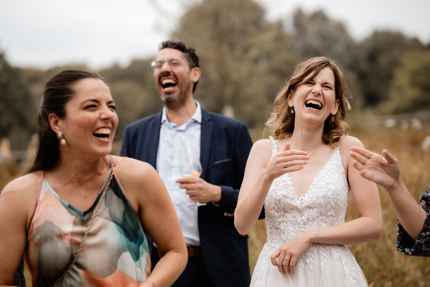 Bride and wedding guests laughing joyfully together outdoors during a wedding celebration.
