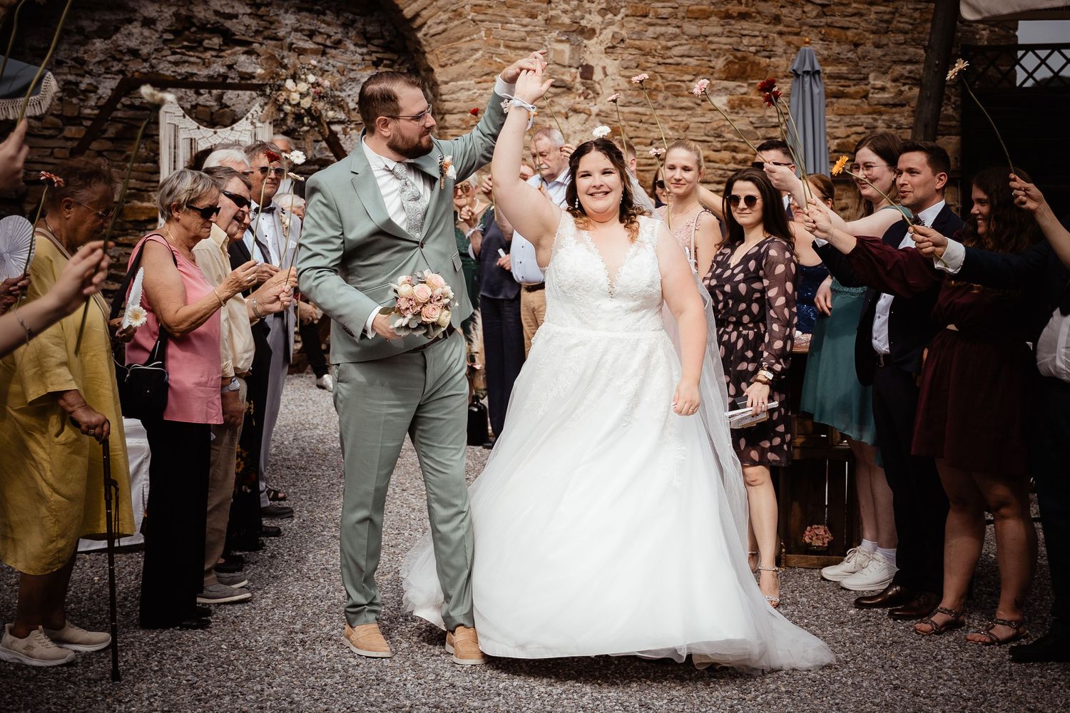 Joyful bride and groom celebrate their recessional as wedding guests cheer and applaud outdoors.