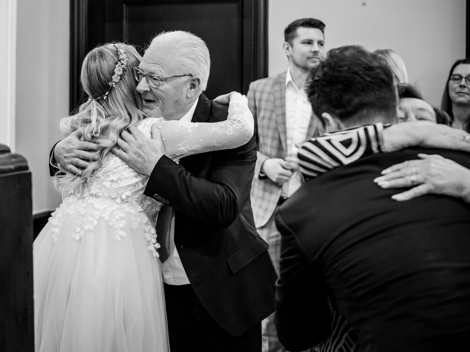Bride in lace wedding dress embracing older gentleman at wedding reception in black and white photo.