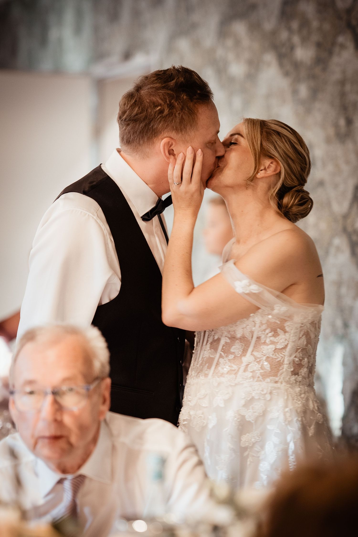 Bride tenderly kisses groom while holding his face during wedding reception dinner.