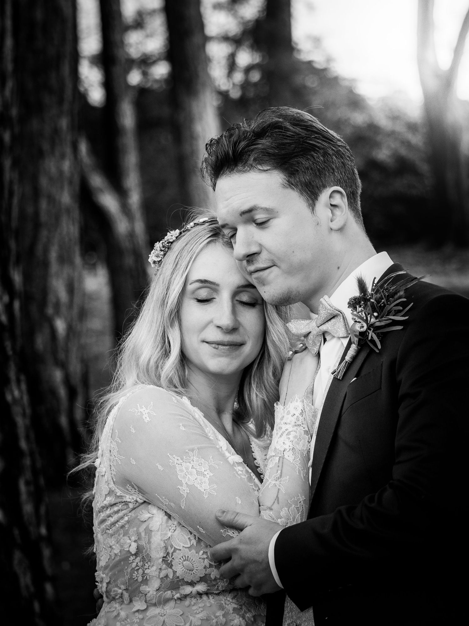 Romantic black and white wedding portrait of bride and groom embracing peacefully among tall forest trees.
