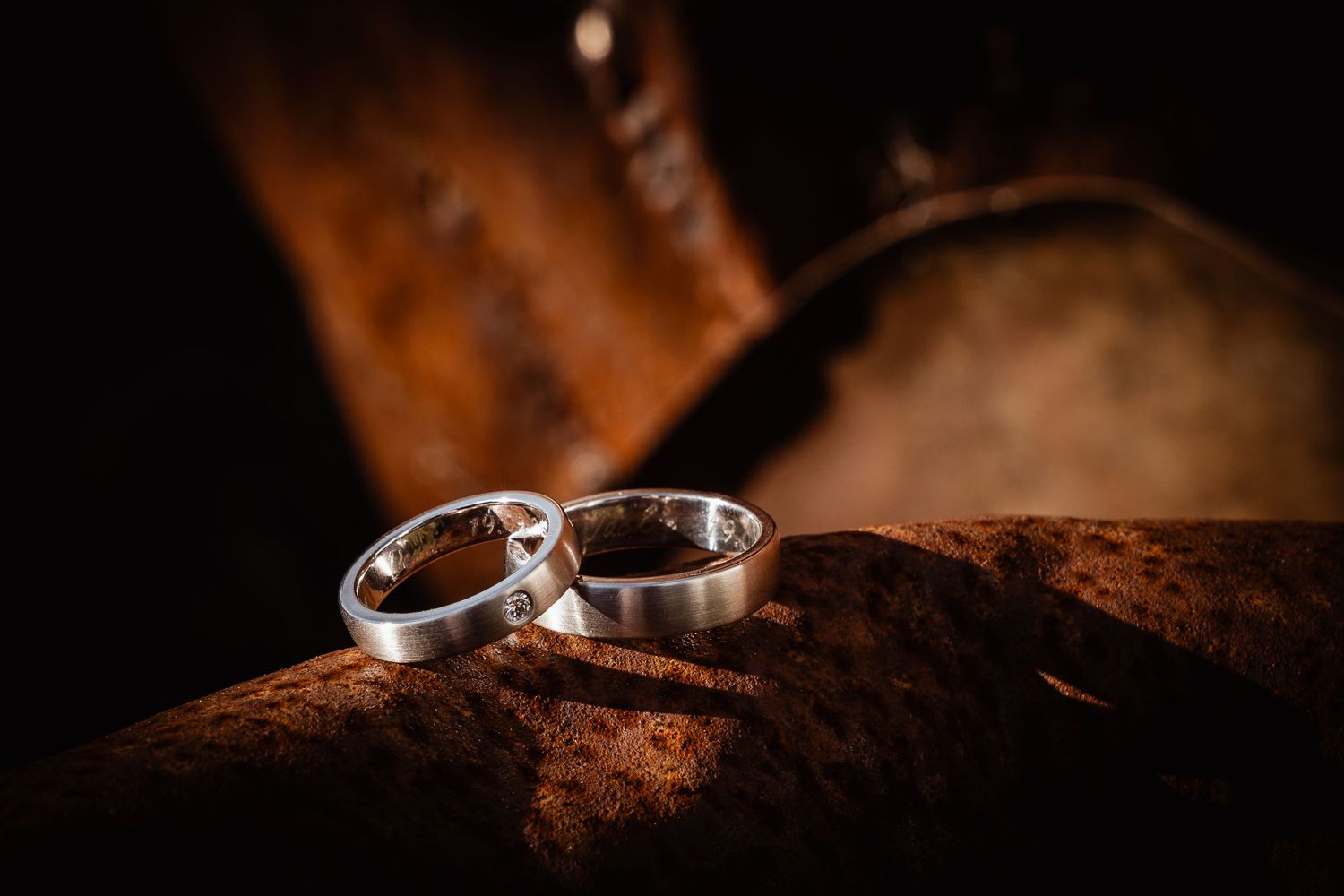 Two silver wedding bands resting on rustic wooden surface in dramatic lighting.