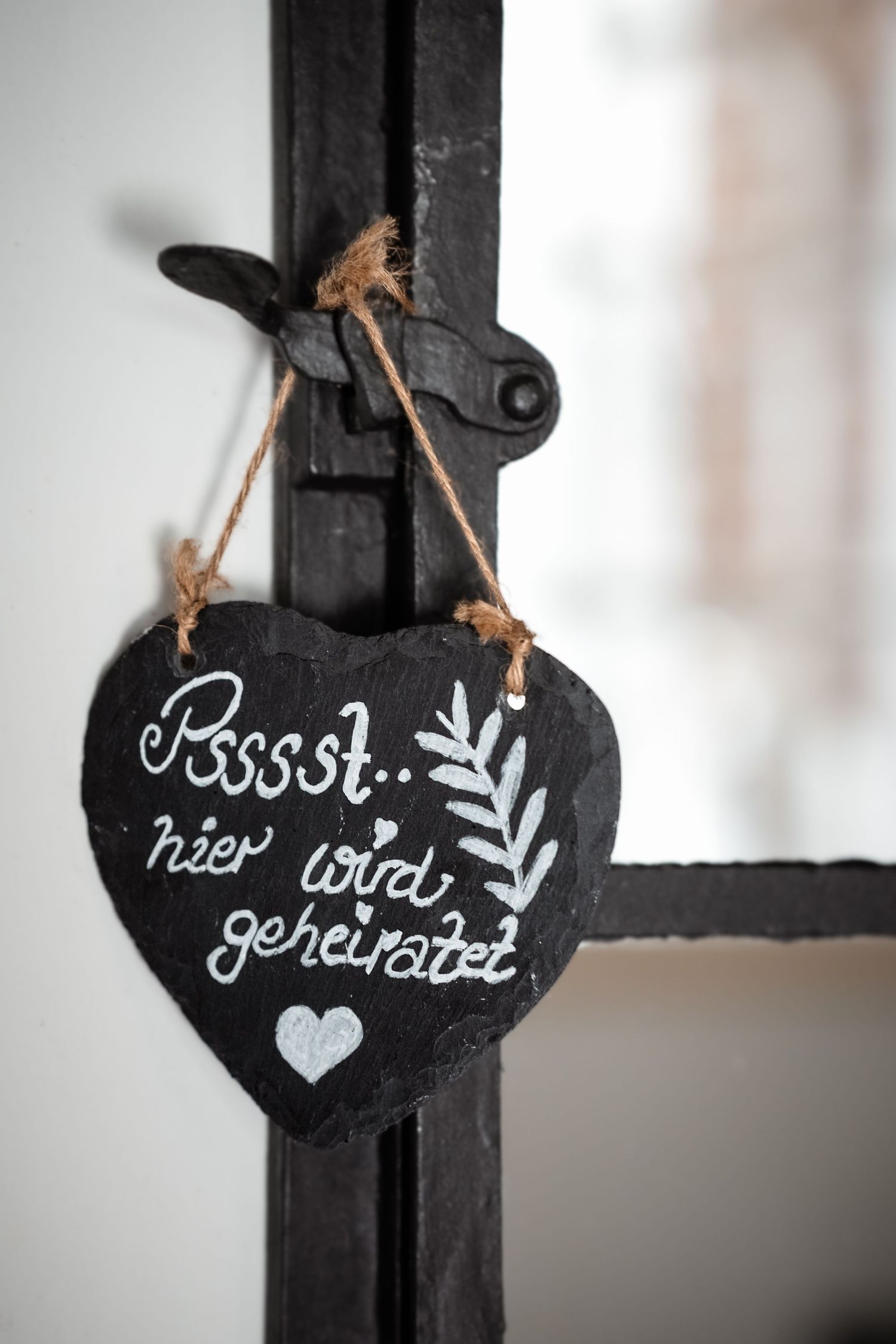 Heart-shaped slate sign with German text Psssst hier wird geheiratet hanging on black iron gate.