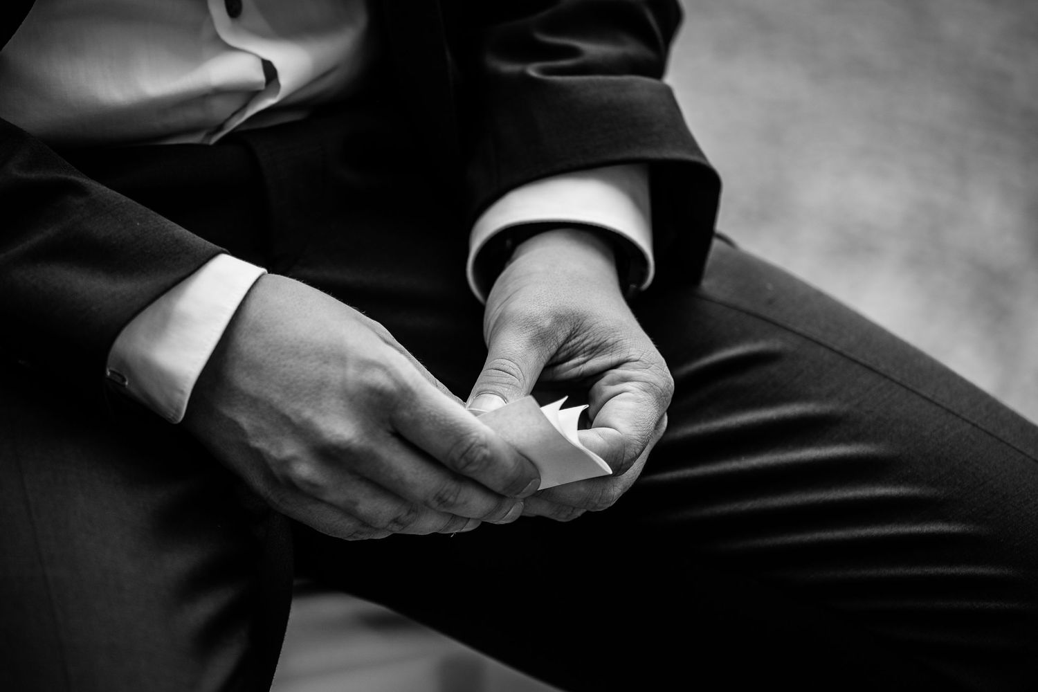 Black and white close-up of groom adjusting cufflinks on his dark suit jacket.