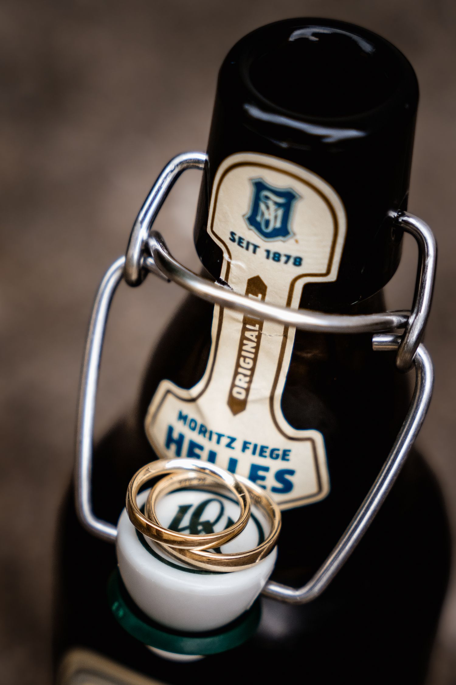 Gold wedding rings resting on Moritz Fiege Helles beer bottle with swing top cap.