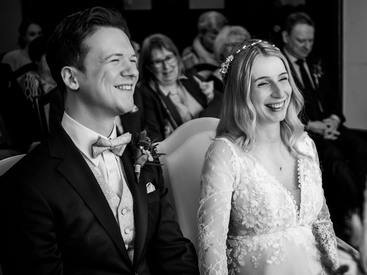 Joyful bride and groom laughing together during wedding ceremony in elegant black and white photo.