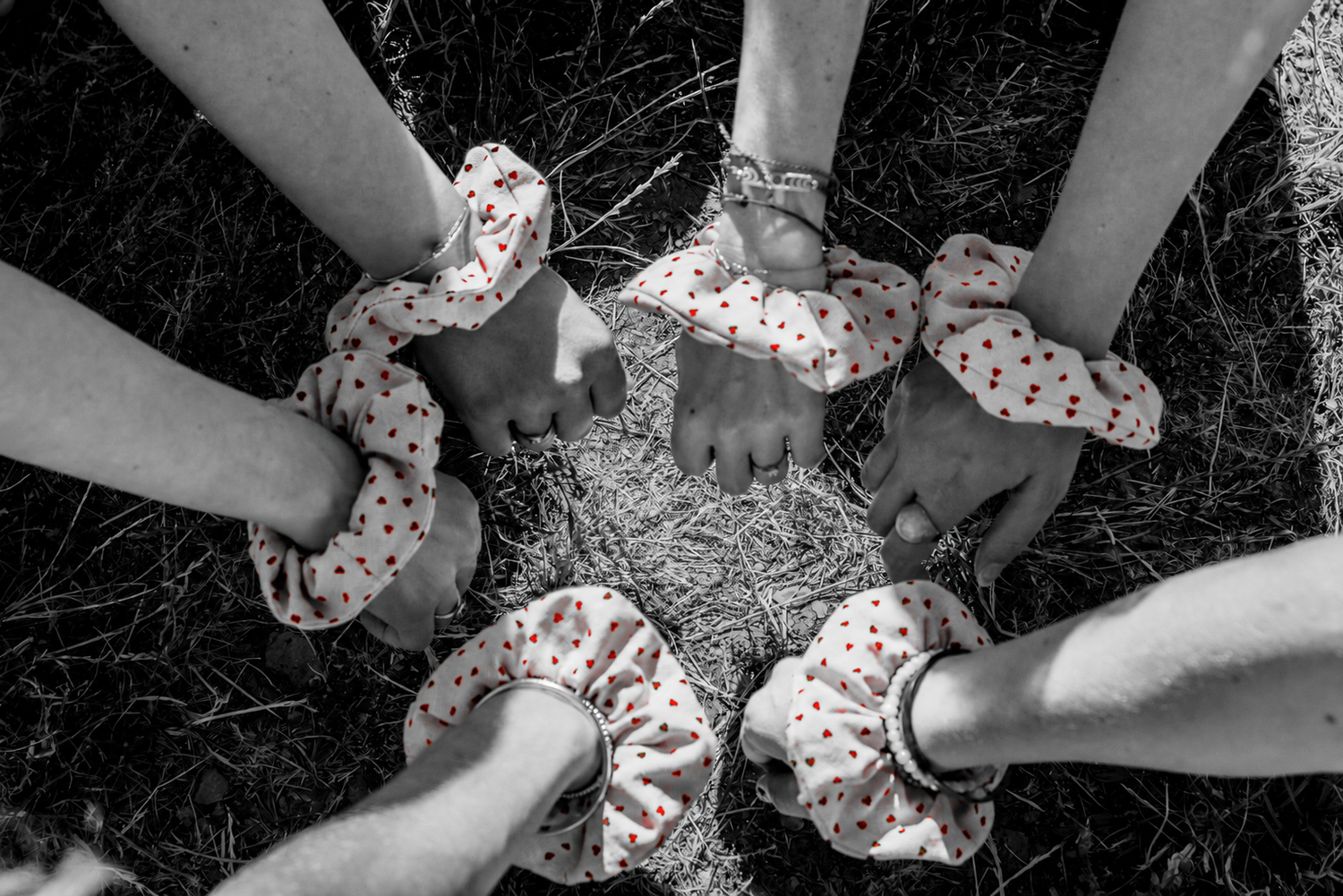 Group of friends with matching polka dot scrunchies on wrists, hands gathered together in circle on grass.