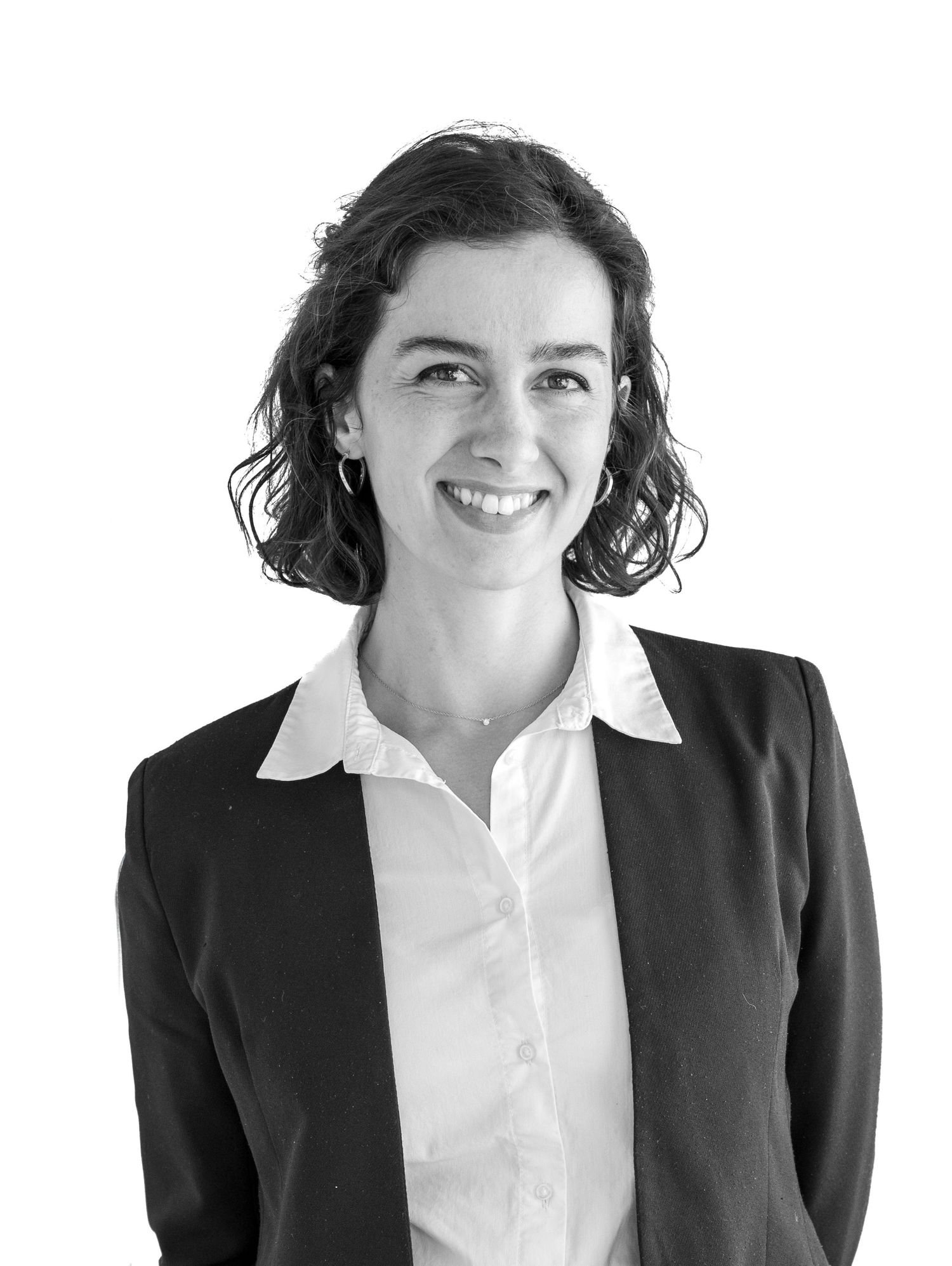 Professional woman in black blazer and white blouse smiling confidently against white background.