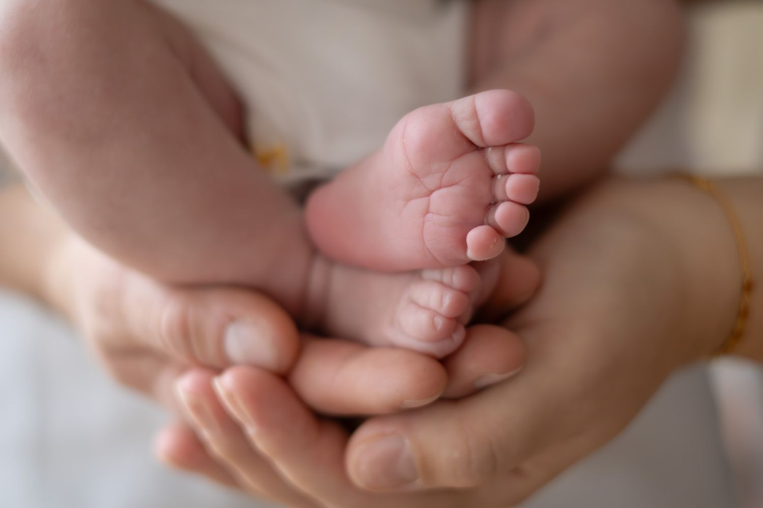 Détail des pieds de bébé dans les mains de ses parents, séance naissance naturelle dans le studio à L'Arbresle ( ouest lyonnais)