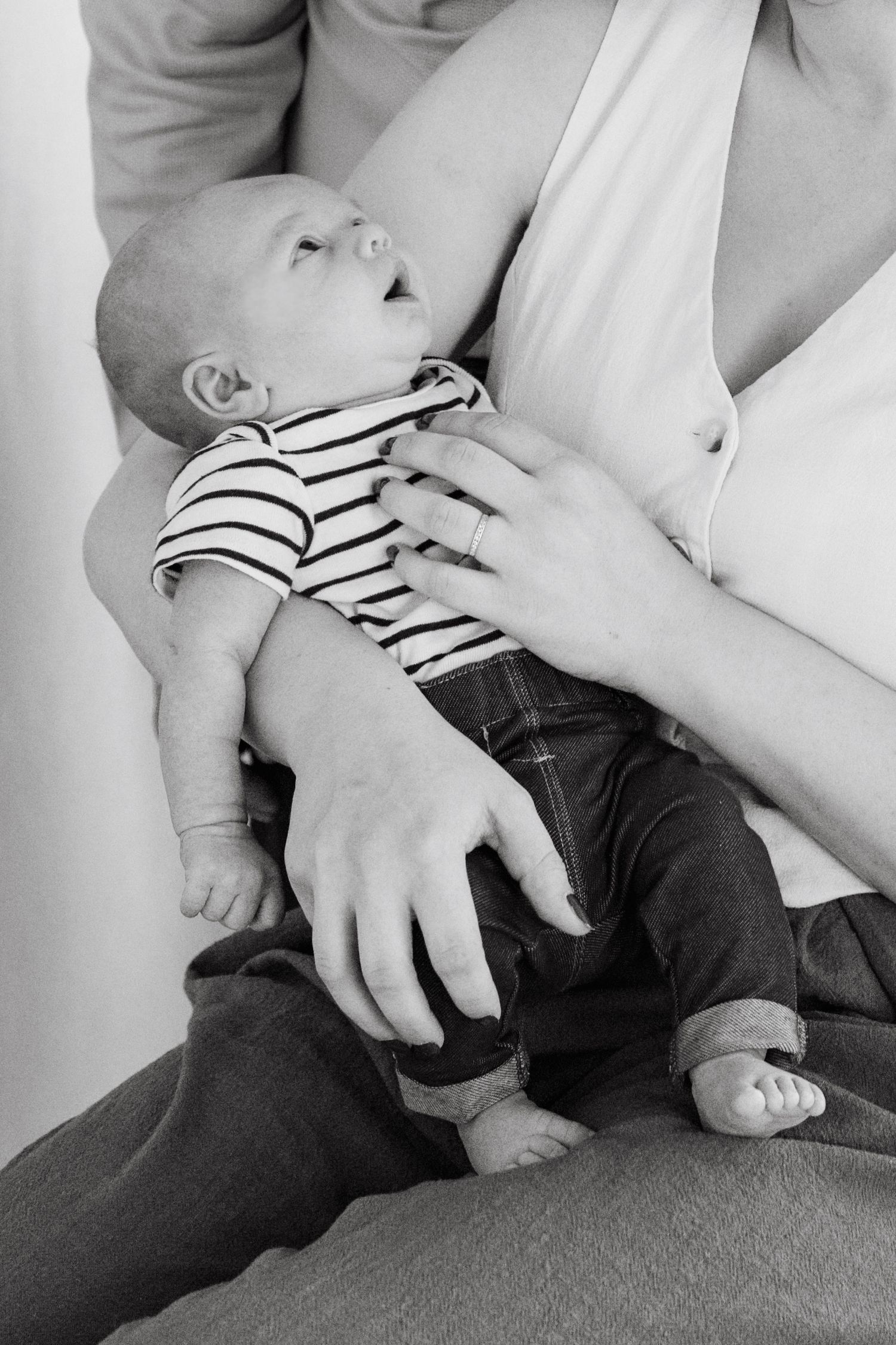 Black and white photo of a newborn baby in striped onesie cradled in mother's arms.
