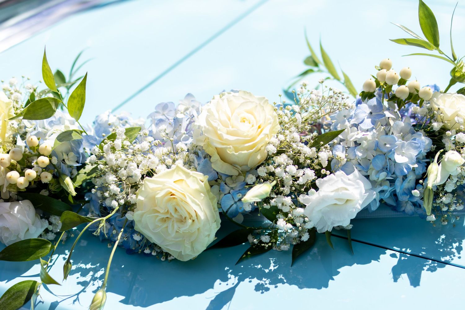 White roses, hydrangeas, and baby's breath floral arrangement on a light blue surface for a wedding.