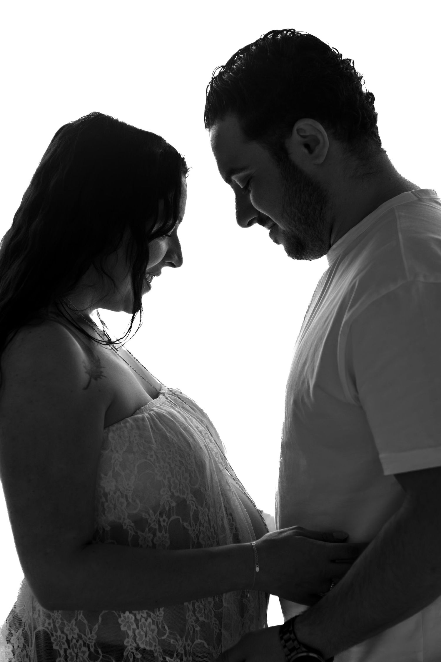 Black and white silhouette of a couple holding a pregnant belly, sharing a tender moment together.