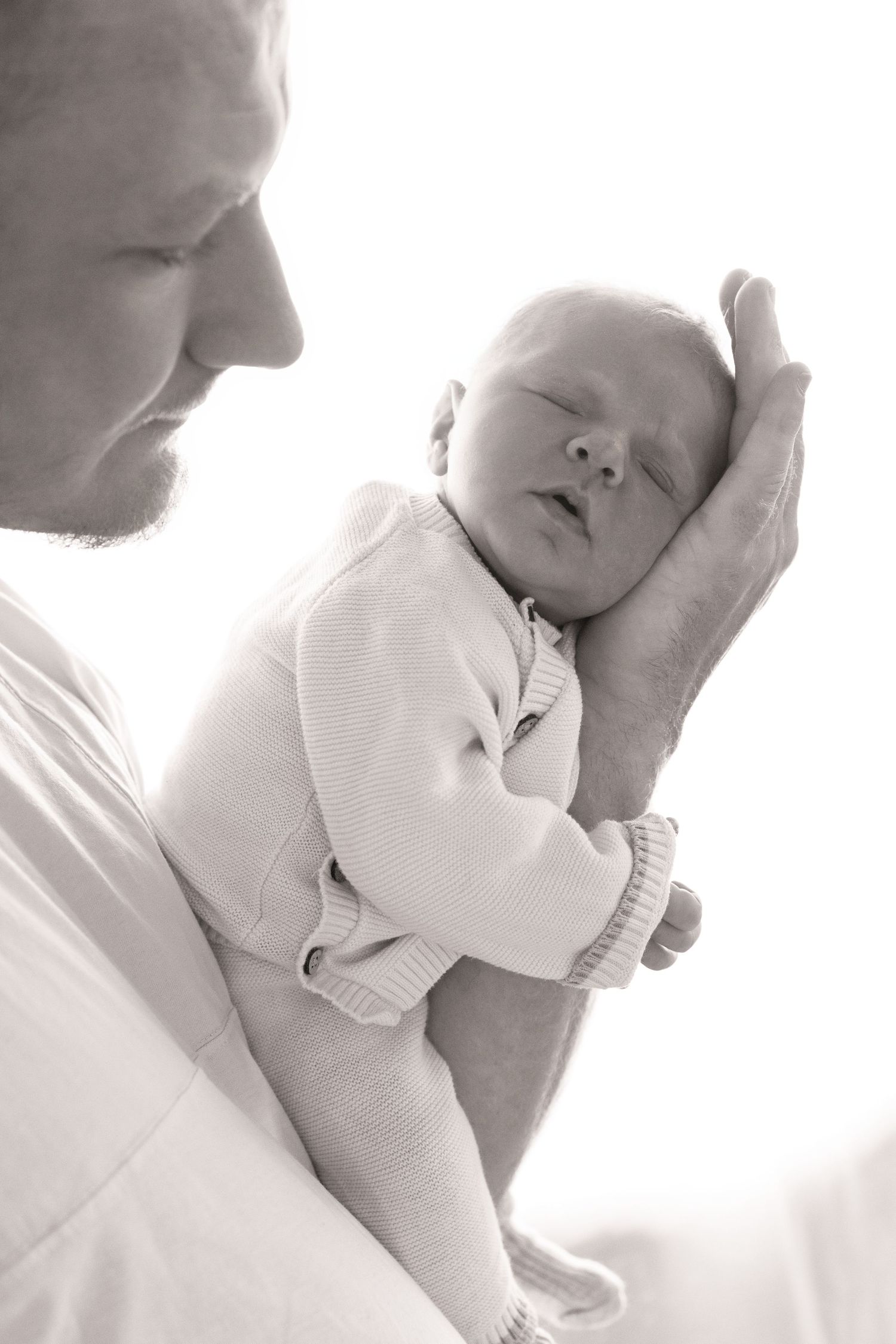 Black and white photo of a father cradling his sleeping newborn baby in his hands.