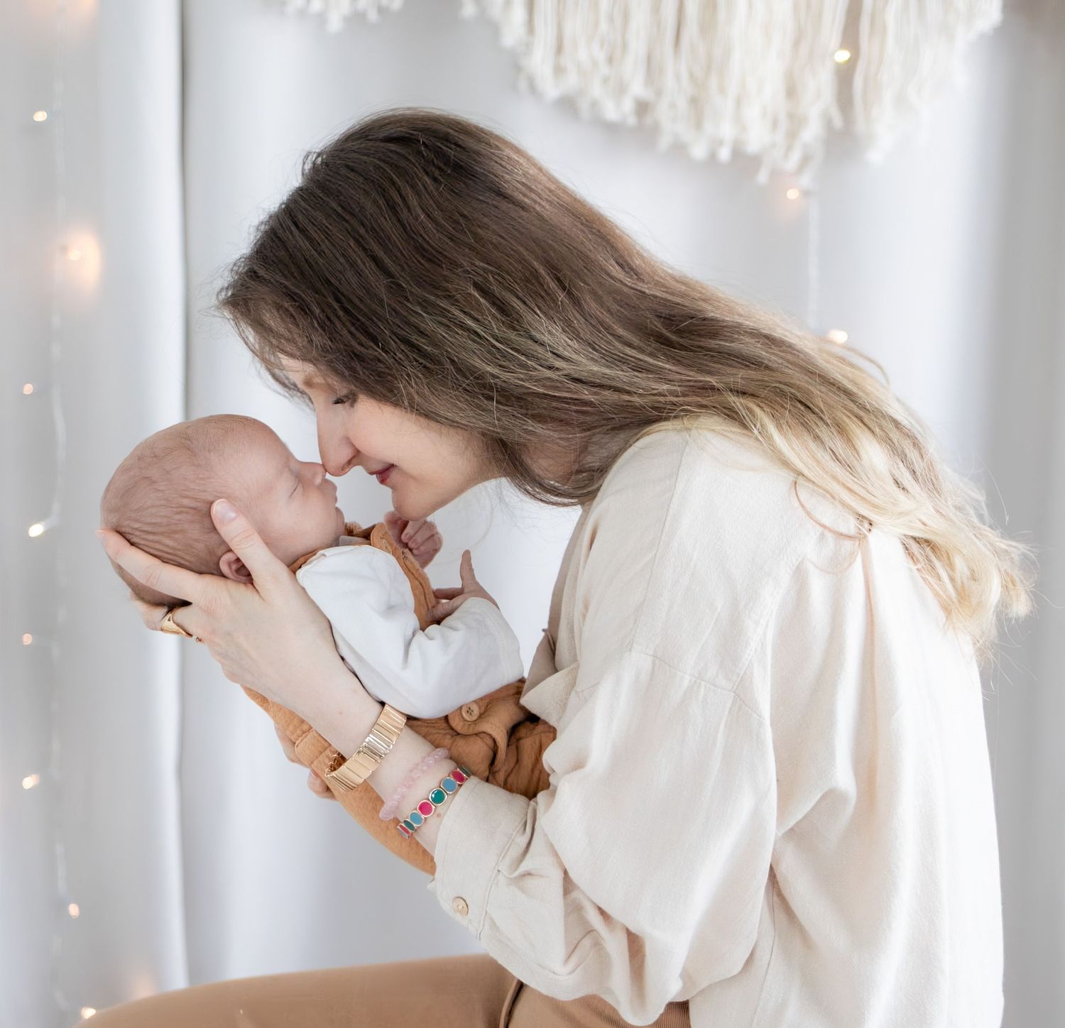A tender mother gently holds her newborn baby close, touching noses in a loving embrace against a soft white backdrop.