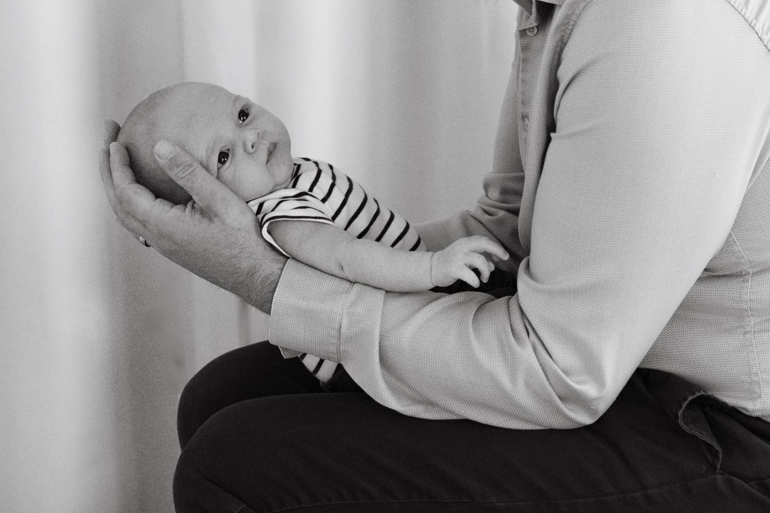 Black and white photo of a newborn baby cradled in an adult's arms, wearing a striped onesie.