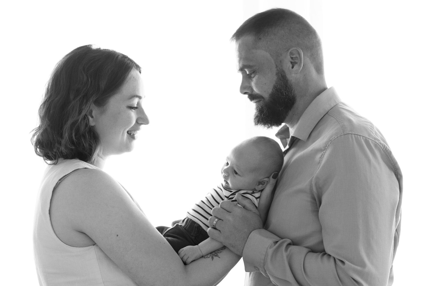 Black and white photo of parents lovingly holding their newborn baby together in a bright studio setting.