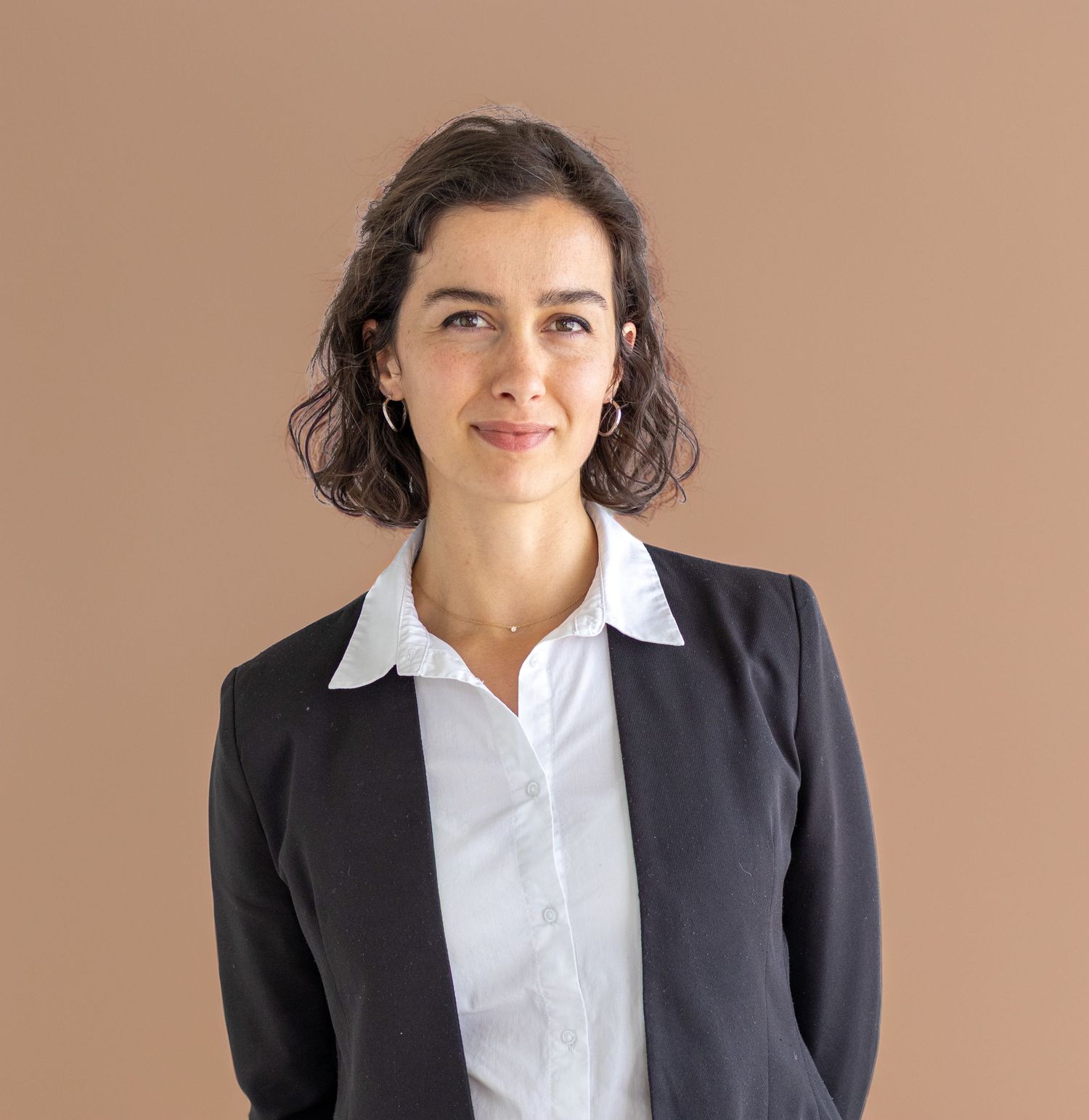 Professional woman in black blazer and white shirt smiling confidently against a warm beige background.