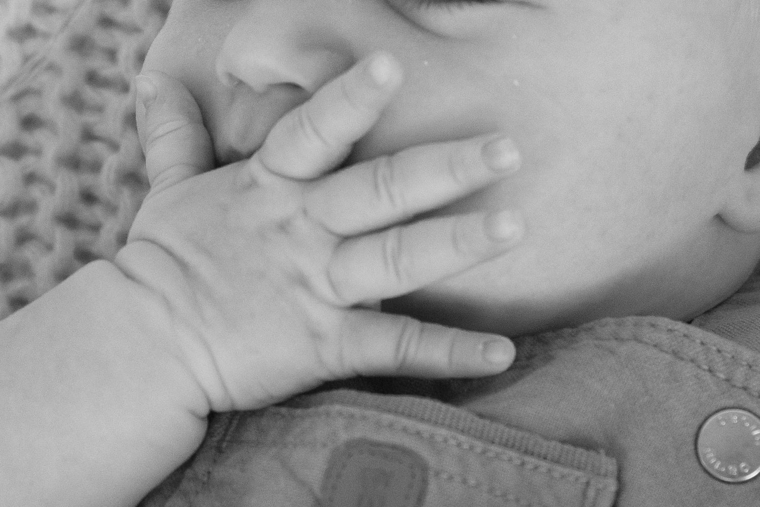 Black and white close-up photo of a baby's tiny hand resting gently on an adult's chest.