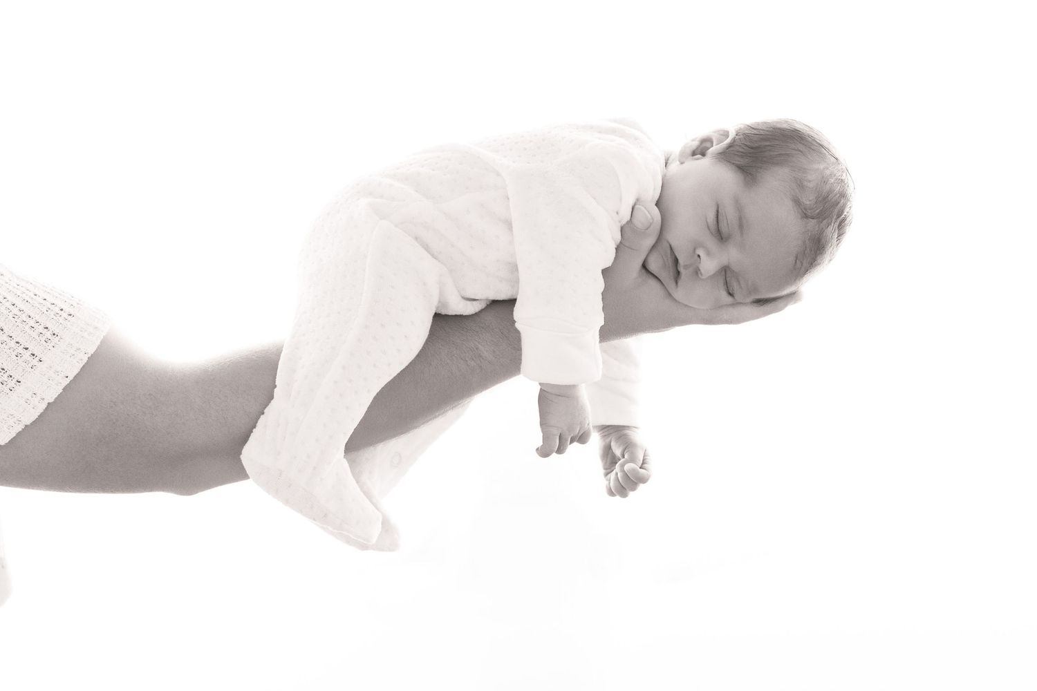 Black and white photo of a sleeping newborn baby cradled in an adults hands against white background.