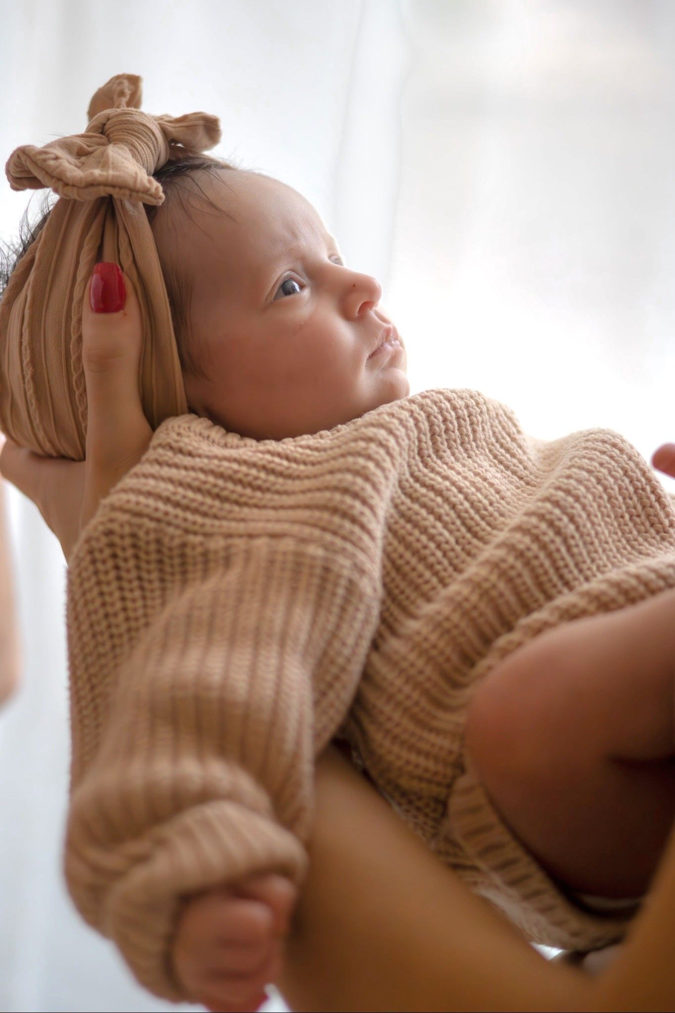 Baby in knit sweater with bow accessory resting on white background.