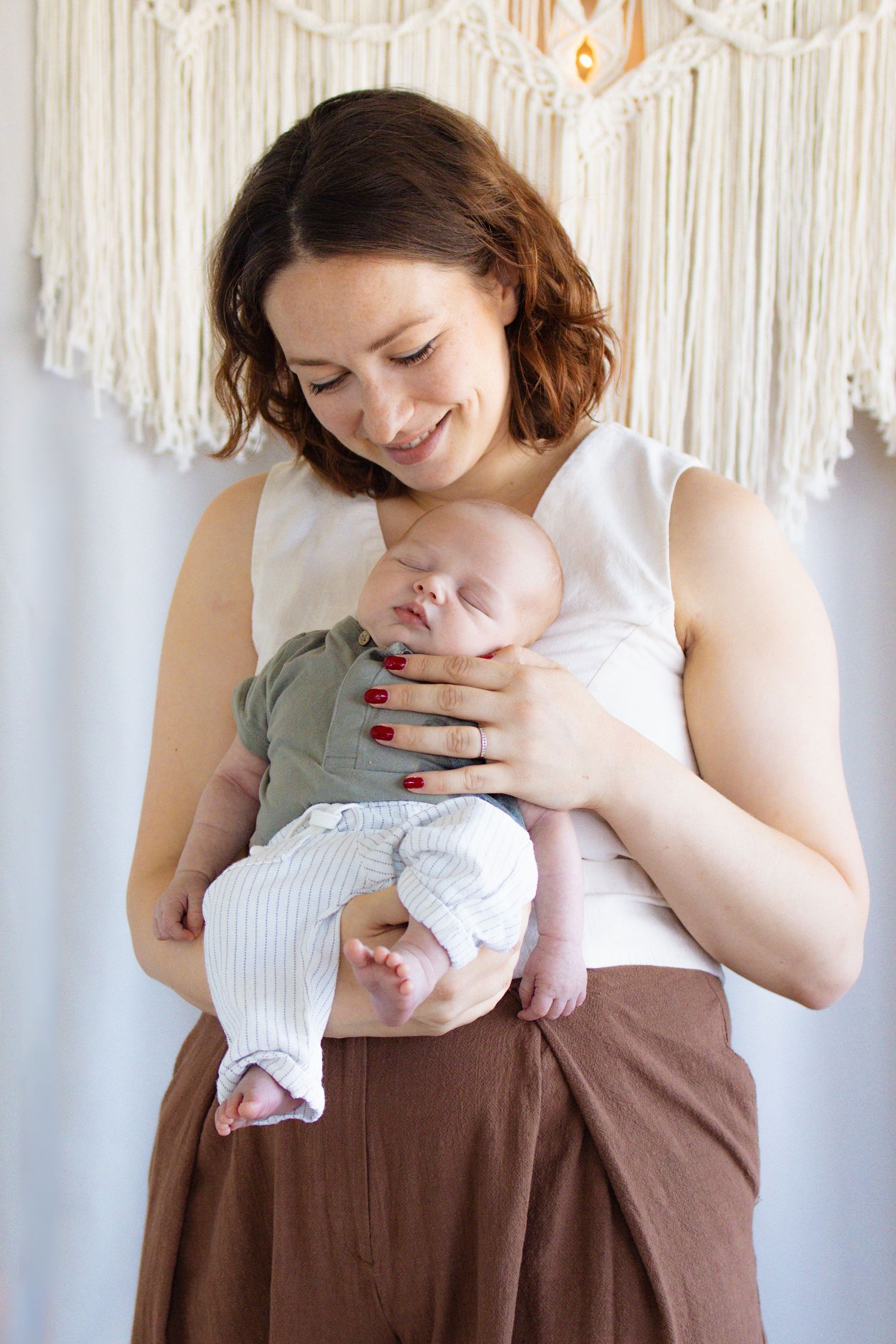 Smiling young mother holding her sleeping newborn baby dressed in green onesie and striped pants.