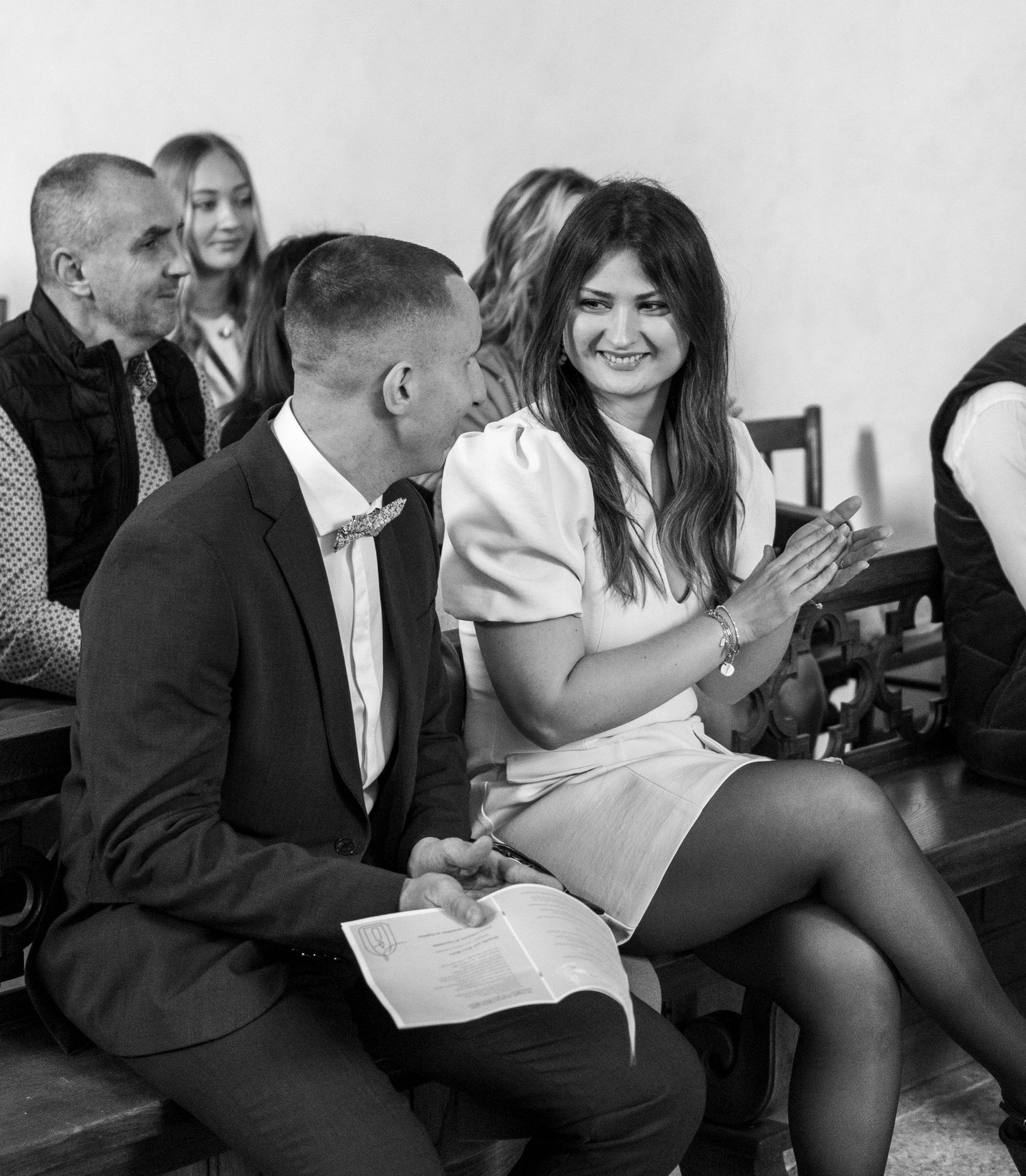 Black and white photo of a couple smiling and conversing at a formal event, seated among other guests.