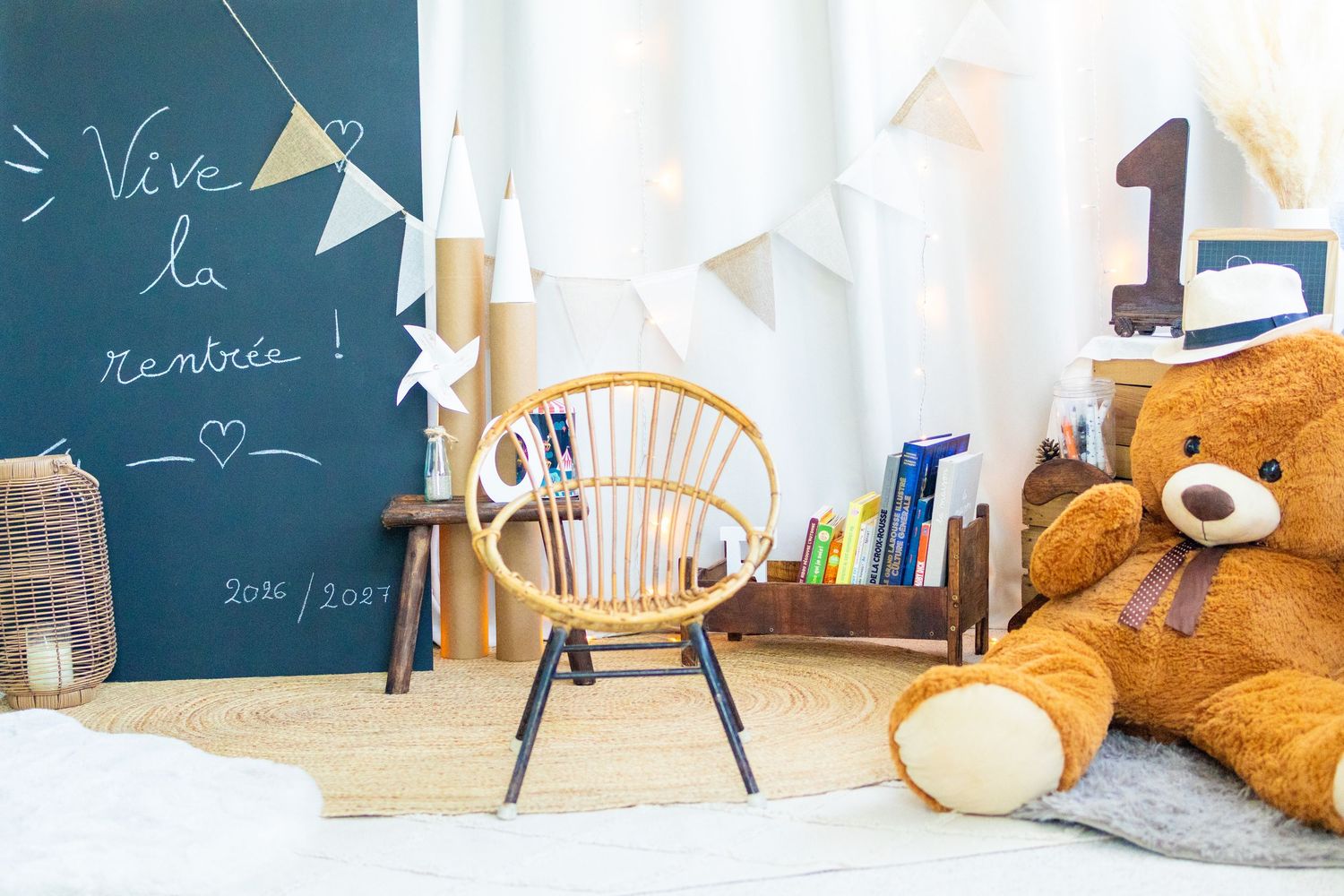 Cozy children's room with a chalkboard, wicker chair, large teddy bear, bunting, and a wooden shelf with books.