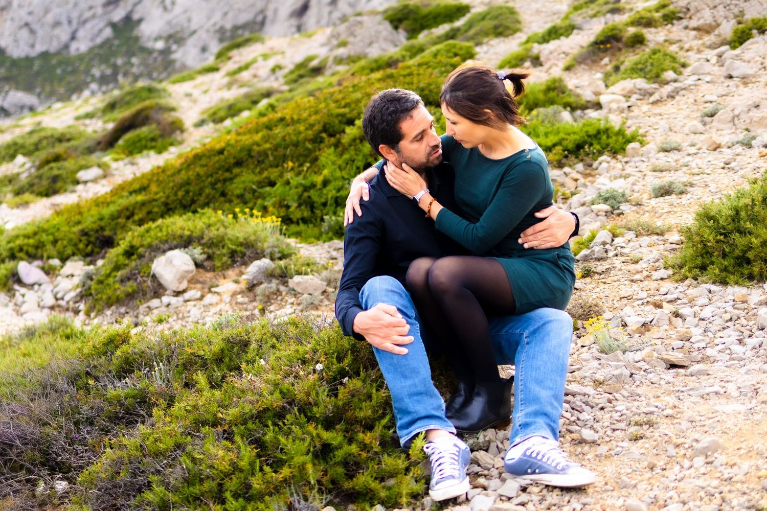 Romantic couple sitting together on rocky mountain terrain, embracing affectionately outdoors.