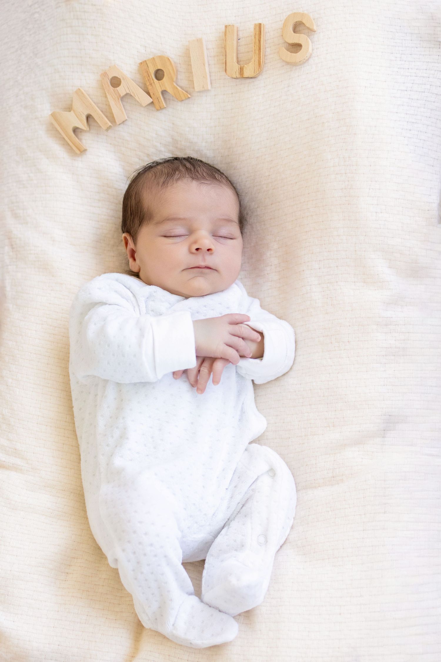 Newborn baby named Marius sleeping peacefully in white onesie on soft blanket with wooden name letters above.