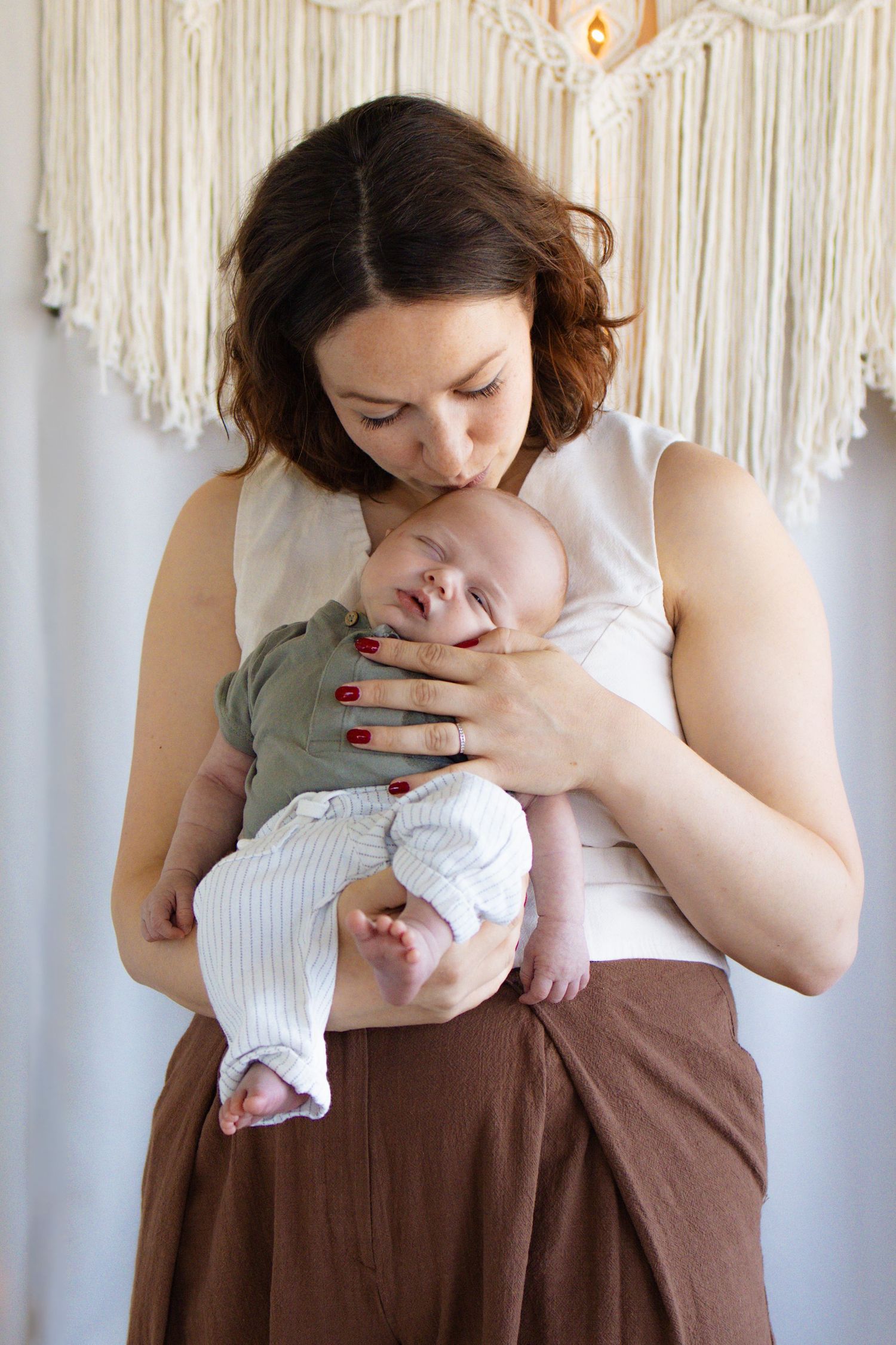 A mother tenderly kisses her newborn baby while cradling them in her arms indoors.