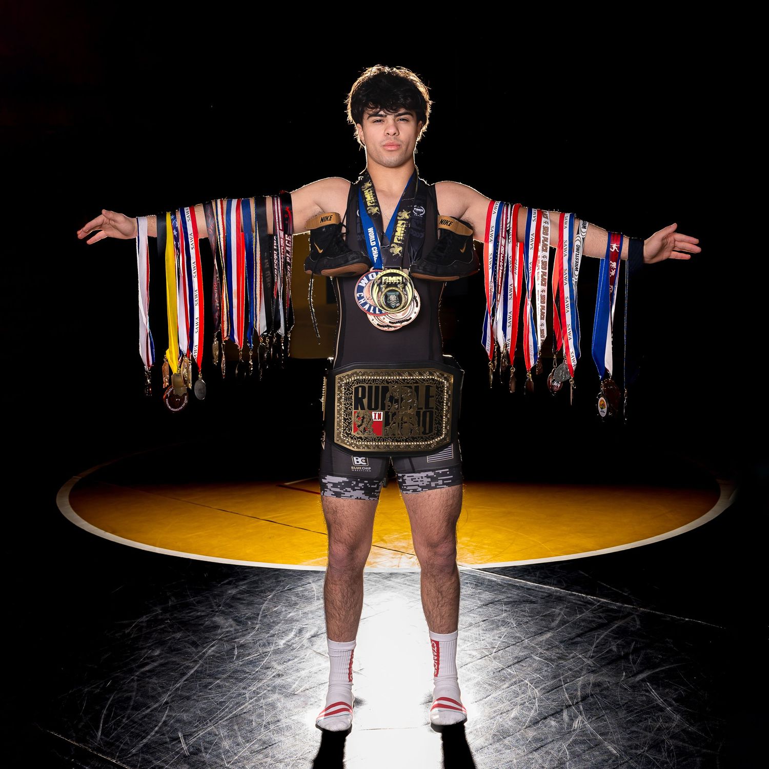 Senior Boy photo of a wrestler in the gym with all his medals draped over his outstretched arms