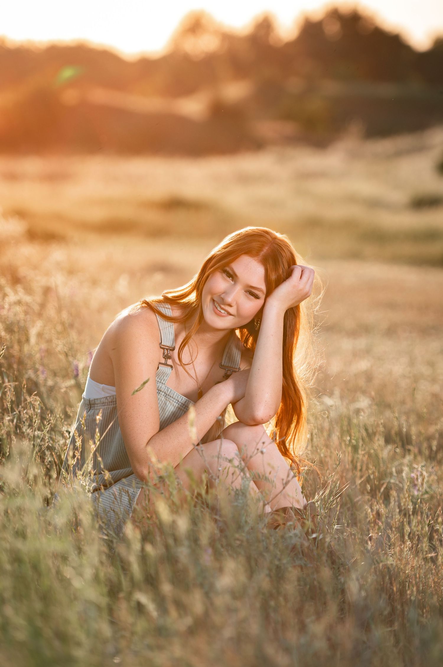 High School Senior sitting in tall grass with a beautiful golden glow from a sunset behind her