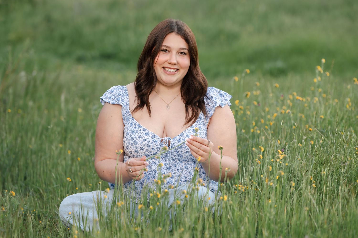 A senior girl sitting in the tall grass with wildflowers at Sailor Bar county park in Fair Oaks, California