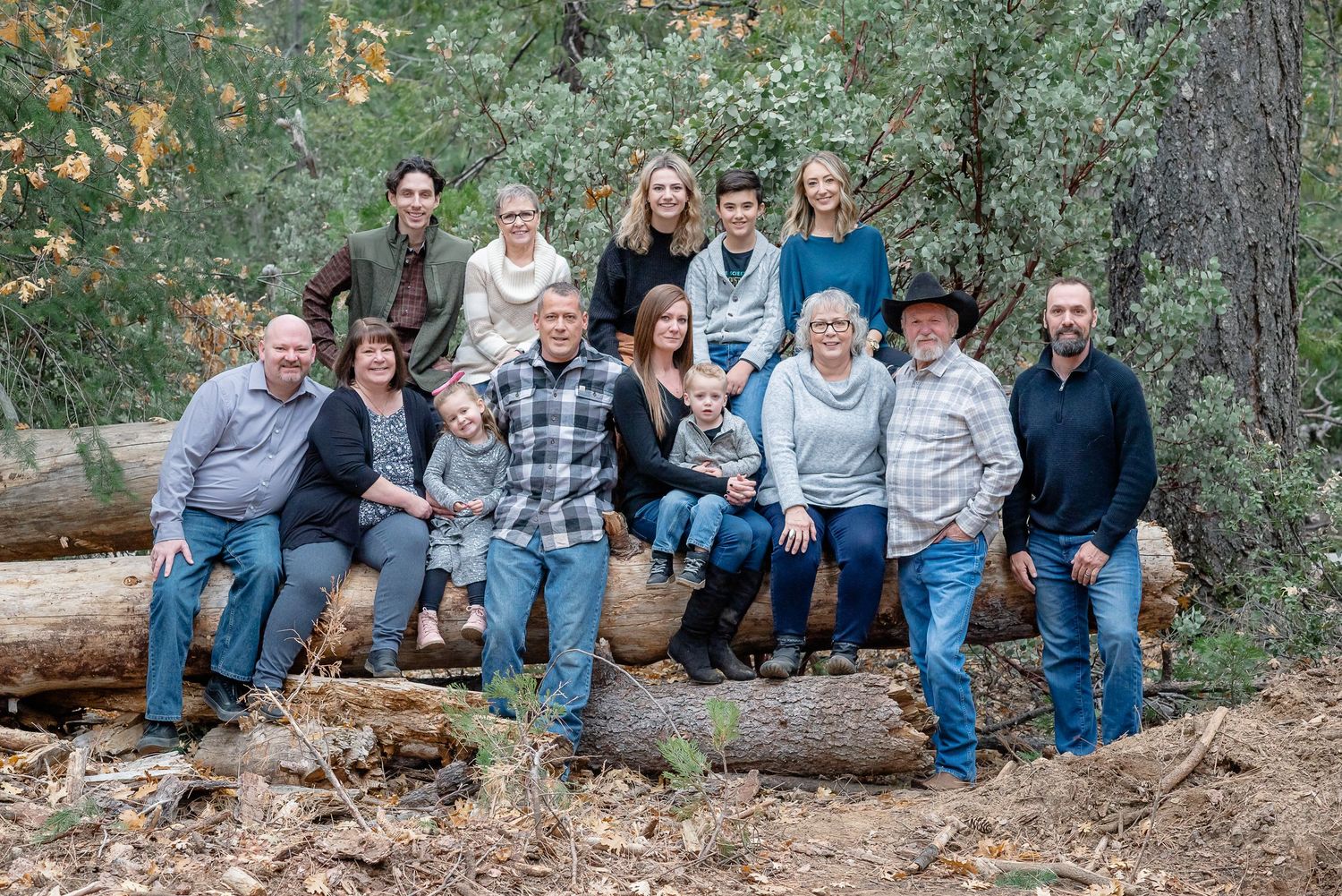 Large family photo taken at their property where they are sitting on downed logs.